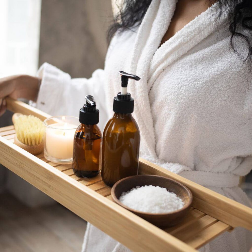 Skincare products on a wooden board held by a lady in a white towelling robe